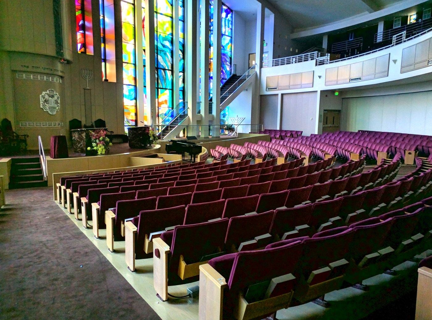A synagogue sanctuary with theater-style seating and tall stained-glass windows